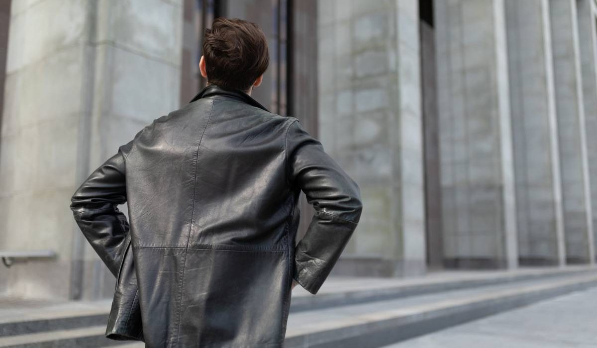 a mature man in a leather jacket is standing looking at the buildings in the city, the view from the back