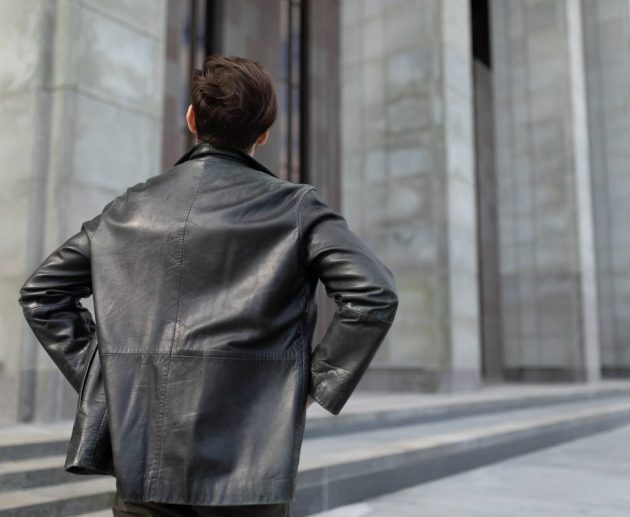 a mature man in a leather jacket is standing looking at the buildings in the city, the view from the back