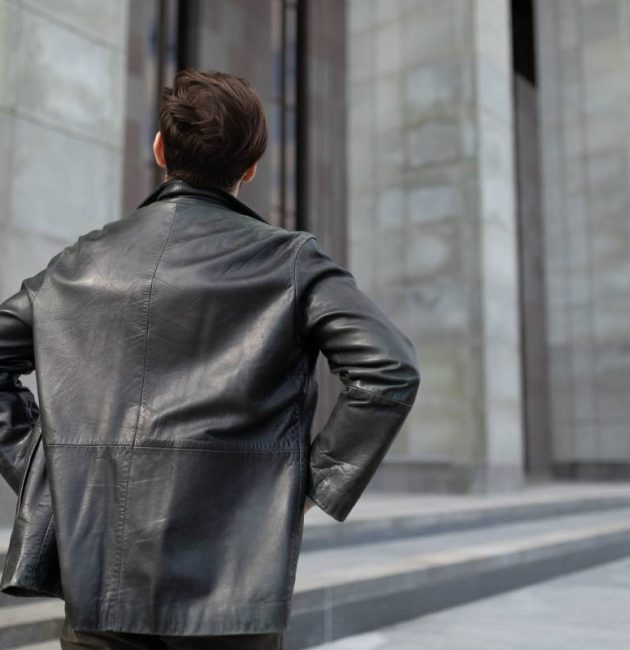 a mature man in a leather jacket is standing looking at the buildings in the city, the view from the back