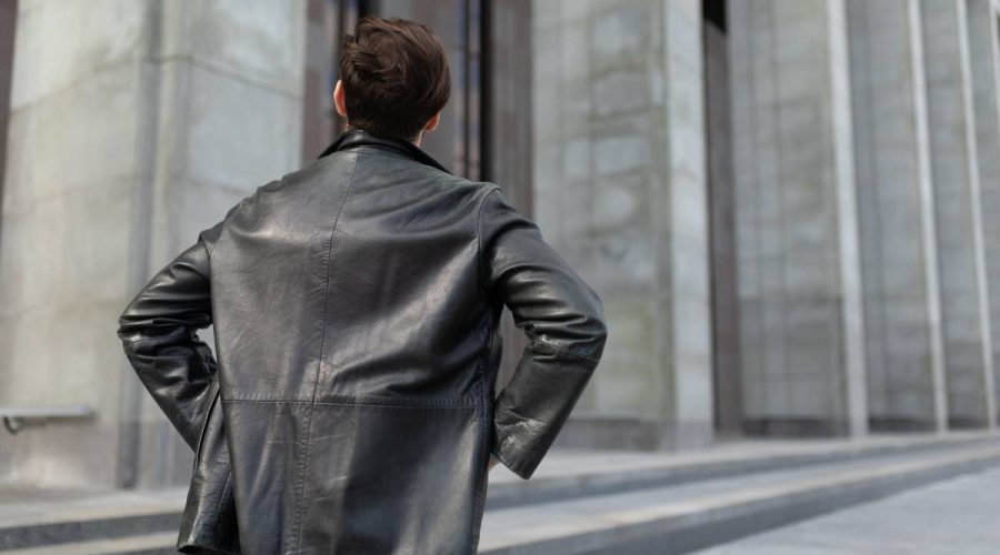 a mature man in a leather jacket is standing looking at the buildings in the city, the view from the back