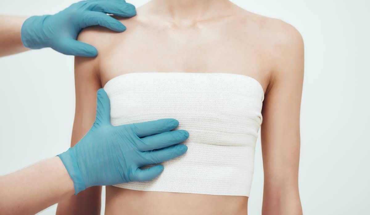 Increase your breast size. Cropped photo of woman waiting for plastic surgery while surgeons in blue medical gloves measuring her breast