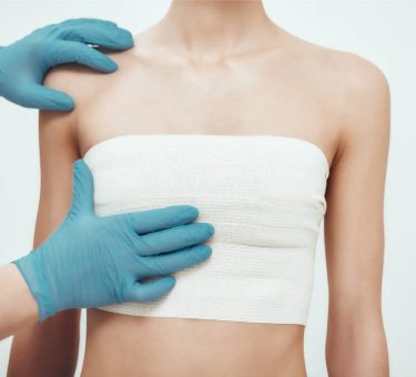 Increase your breast size. Cropped photo of woman waiting for plastic surgery while surgeons in blue medical gloves measuring her breast