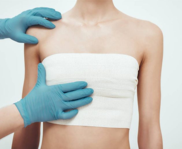 Increase your breast size. Cropped photo of woman waiting for plastic surgery while surgeons in blue medical gloves measuring her breast