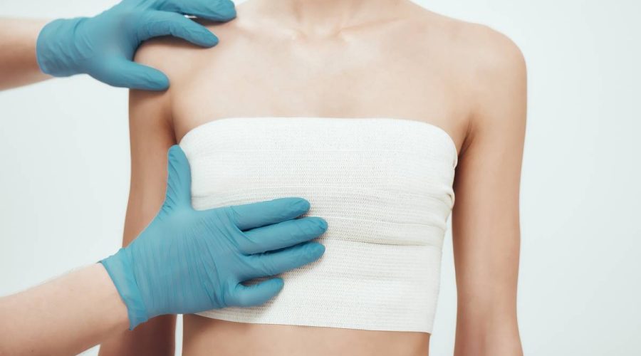 Increase your breast size. Cropped photo of woman waiting for plastic surgery while surgeons in blue medical gloves measuring her breast