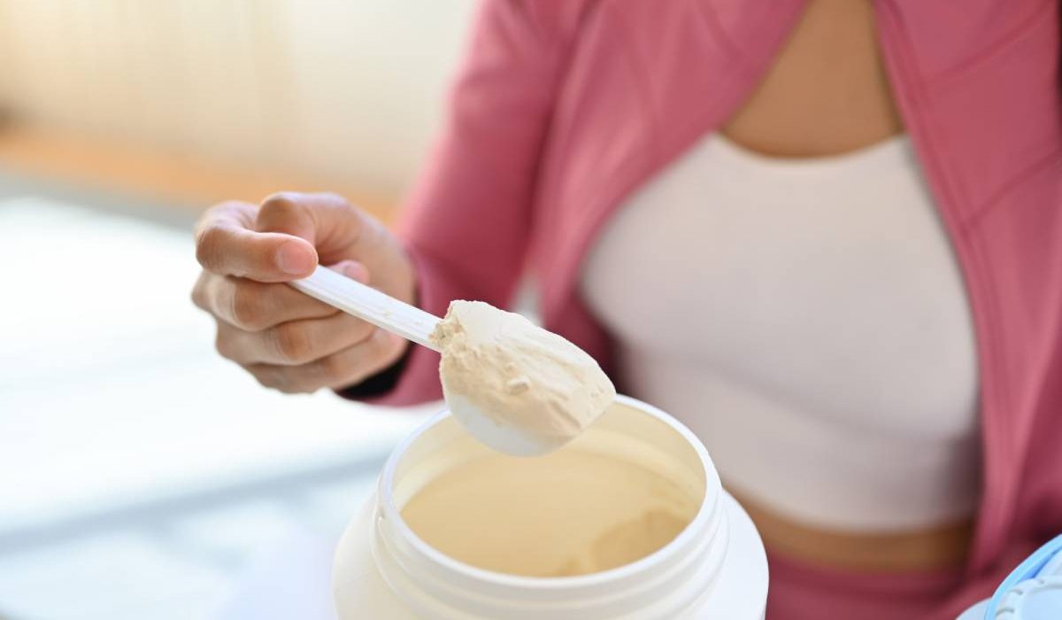 Young woman in sportswear hand holding scoop making protein shake after morning workout. Healthy lifestyle concept