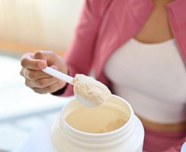 Young woman in sportswear hand holding scoop making protein shake after morning workout. Healthy lifestyle concept