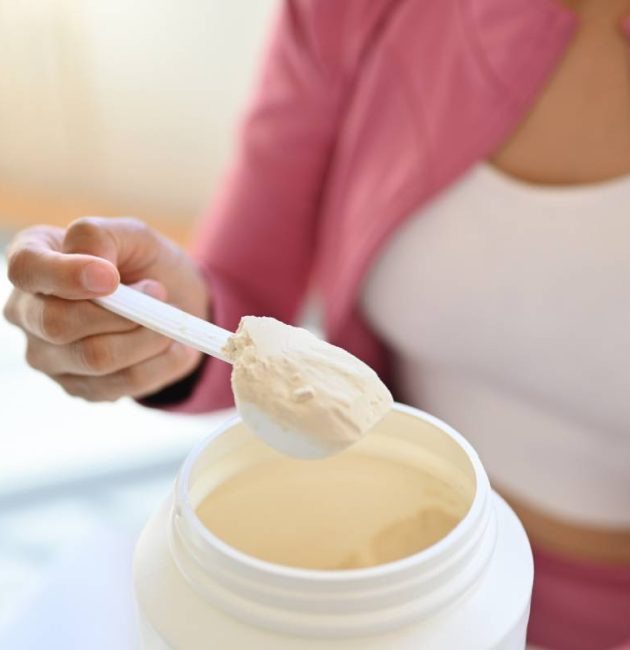 Young woman in sportswear hand holding scoop making protein shake after morning workout. Healthy lifestyle concept