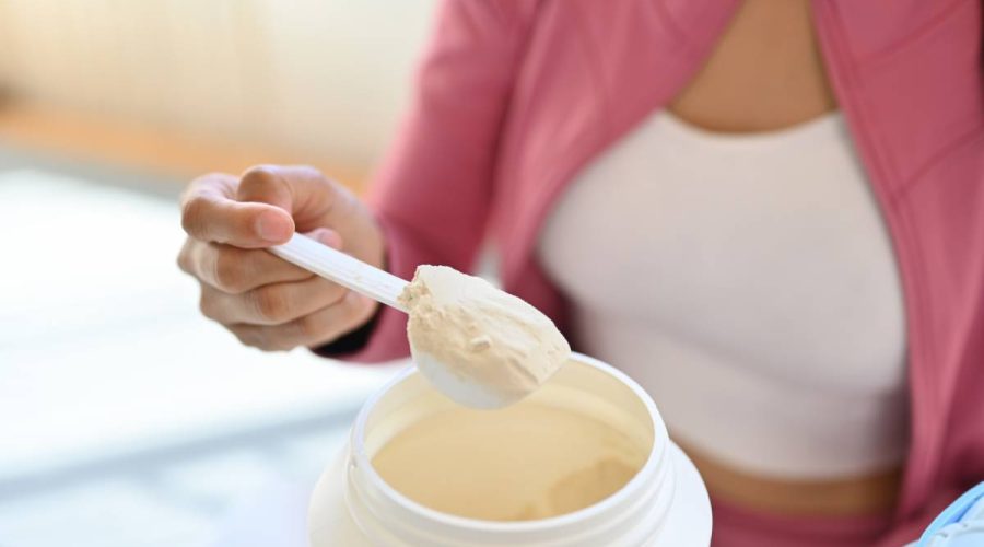 Young woman in sportswear hand holding scoop making protein shake after morning workout. Healthy lifestyle concept